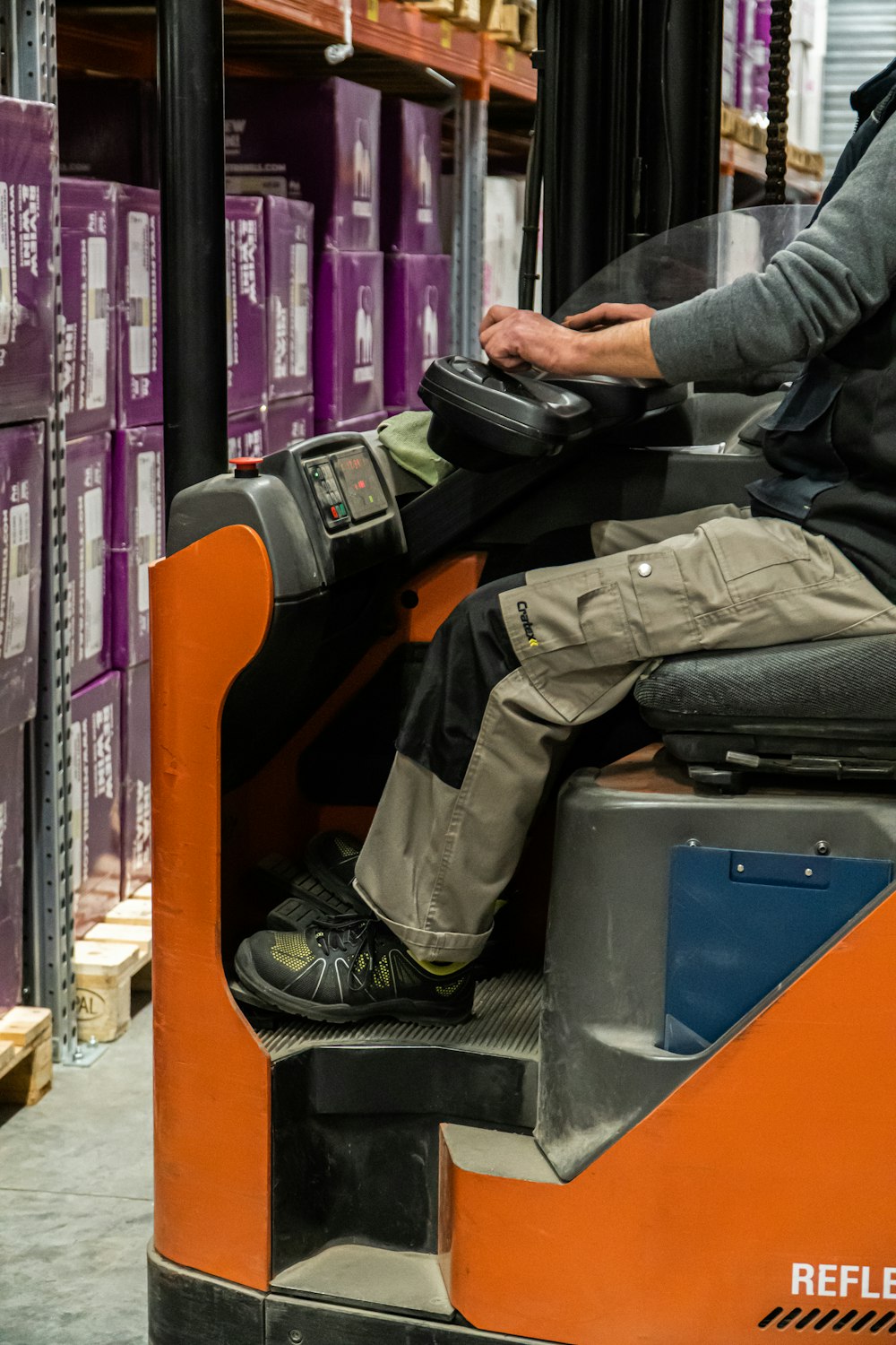 Mann in grauer Jacke und schwarzer Hose sitzt auf orangefarbenem Stuhl