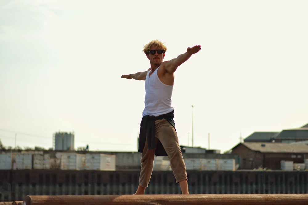 woman in white tank top and brown pants jumping on brown wooden railings during daytime