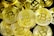 A pile of gold-colored coins with the Bitcoin symbol prominently displayed on each. The coins, with intricate detailing, overlap each other creating a dense, textured surface.