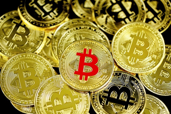 A collection of cryptocurrency coins with the Bitcoin symbol prominently displayed, most of which are gold, except for one coin in the center that features a red Bitcoin symbol.