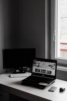 A minimalist workspace with a laptop displaying a clean, elegant website design in black, white, and gold tones.