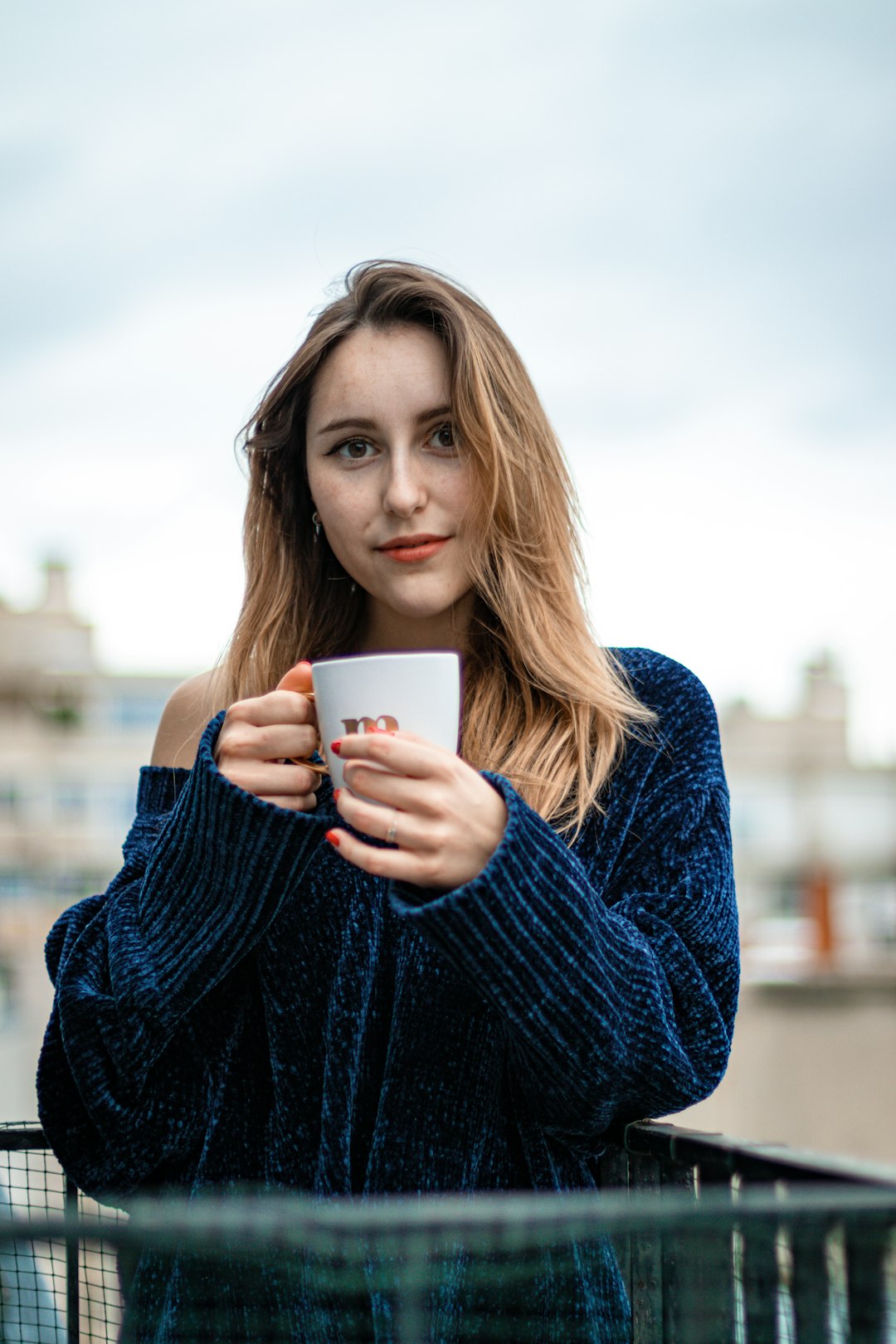 woman in blue sweater holding white ceramic mug