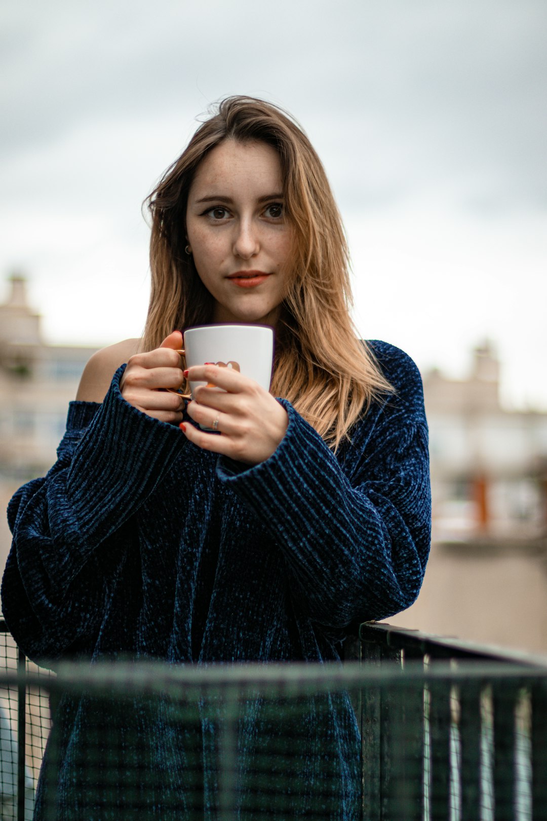 woman in blue sweater holding white ceramic mug