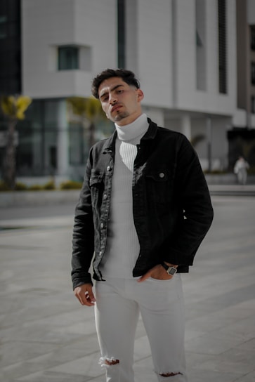 man in black jacket and white pants standing on sidewalk during daytime