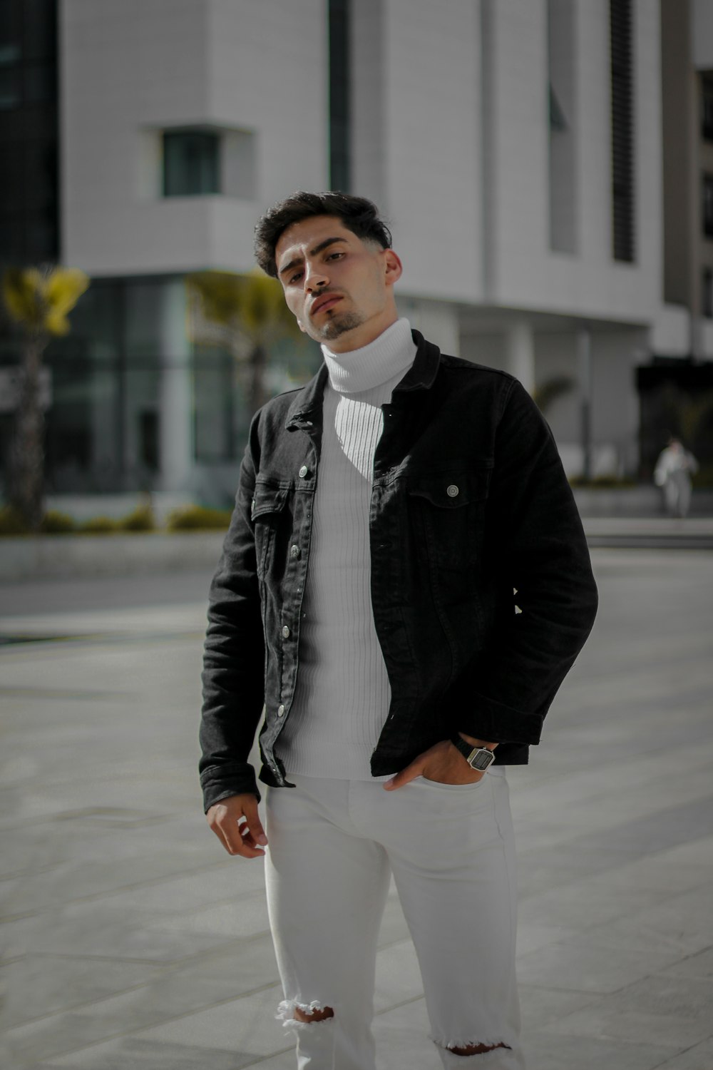 man in black jacket and white pants standing on sidewalk during daytime