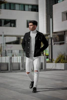 A model wearing a sleek black bomber jacket and white sneakers, walking down a city street.