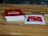 A wooden table features a stack of cards with a red cover labeled 'Exploding Kittens'. Next to it, a single card is laid out showing artwork and text related to the game. The setting is casual and likely related to a tabletop gaming session.