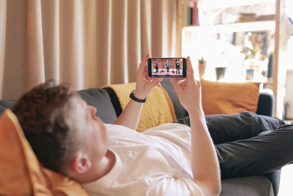 man in black t-shirt lying on bed using smartphone