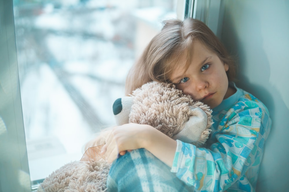 girl in blue white and red plaid shirt hugging brown teddy bear