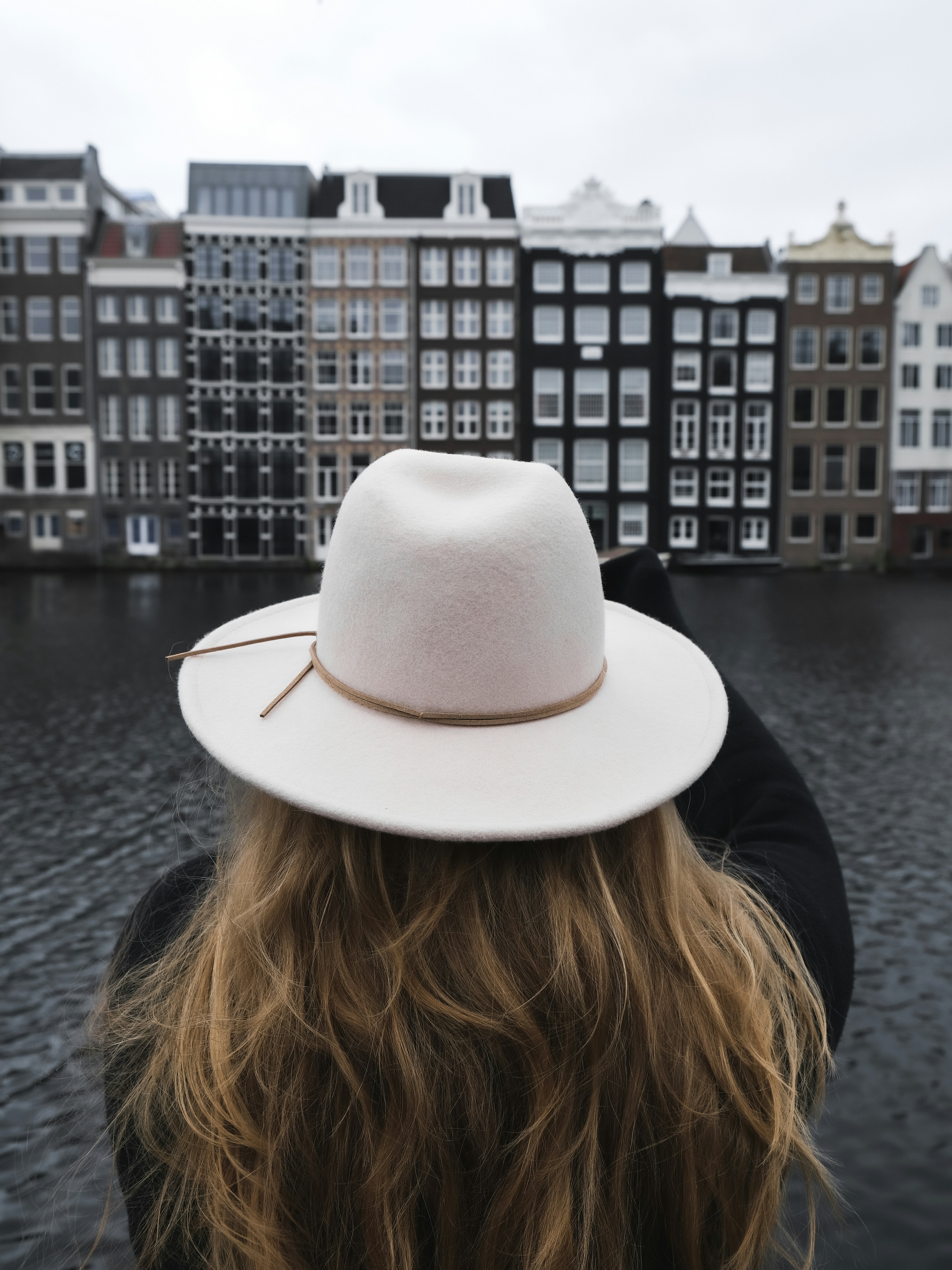 woman in black shirt wearing white fedora hat standing near body of water during daytime