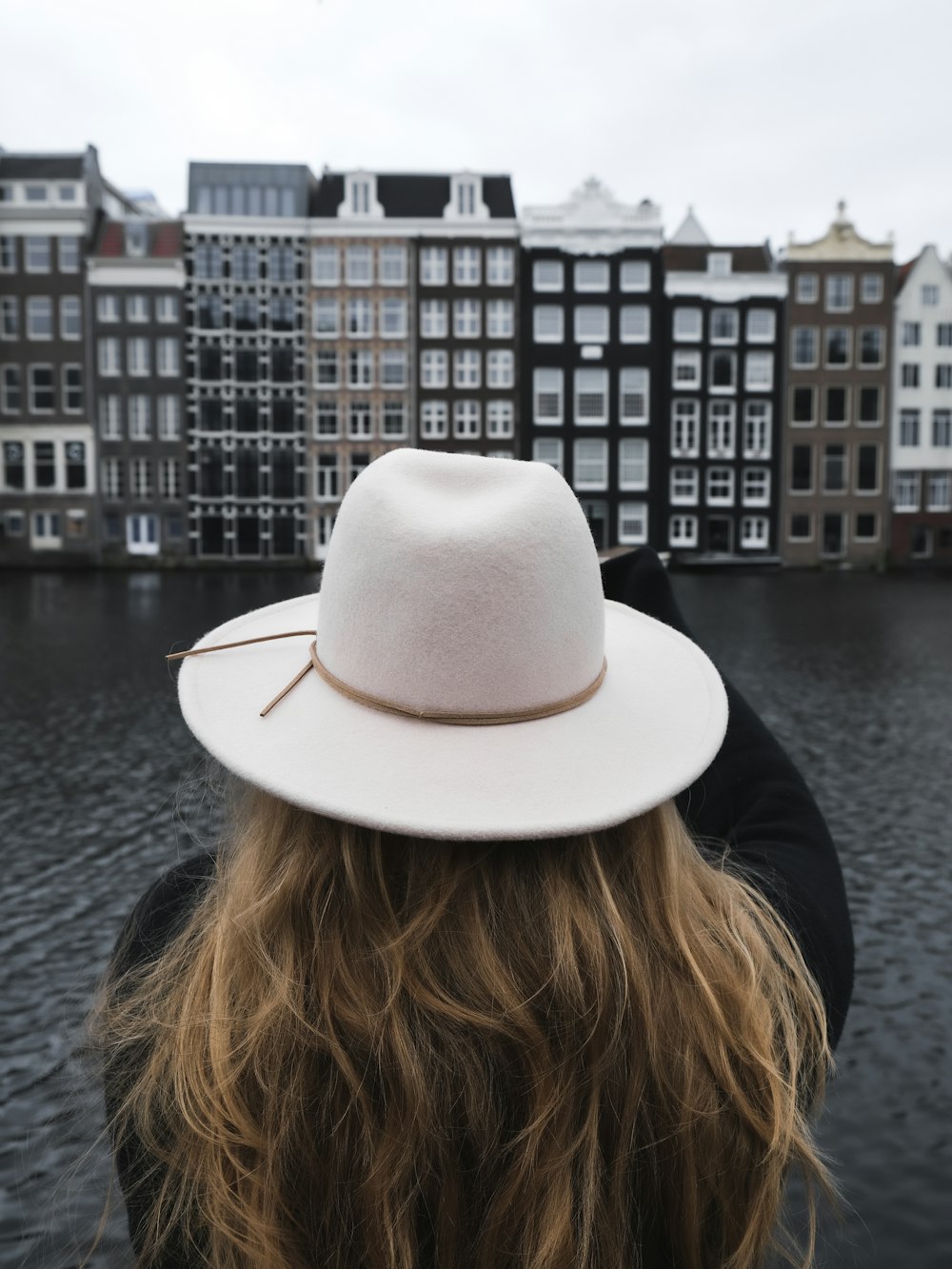 woman in black shirt wearing white fedora hat standing near body of water during daytime