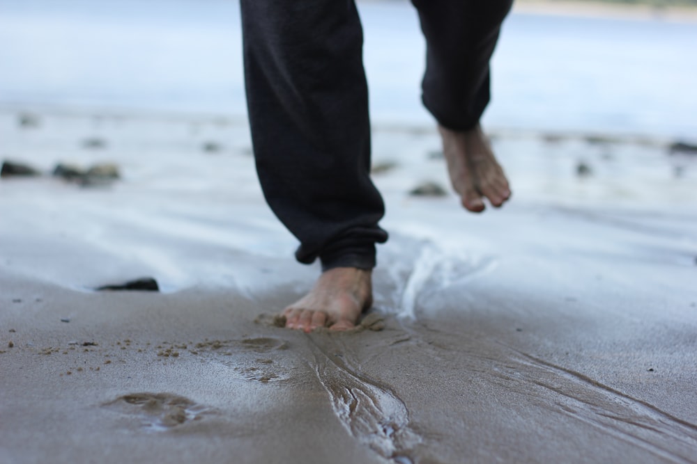 person in black pants standing on gray sand during daytime