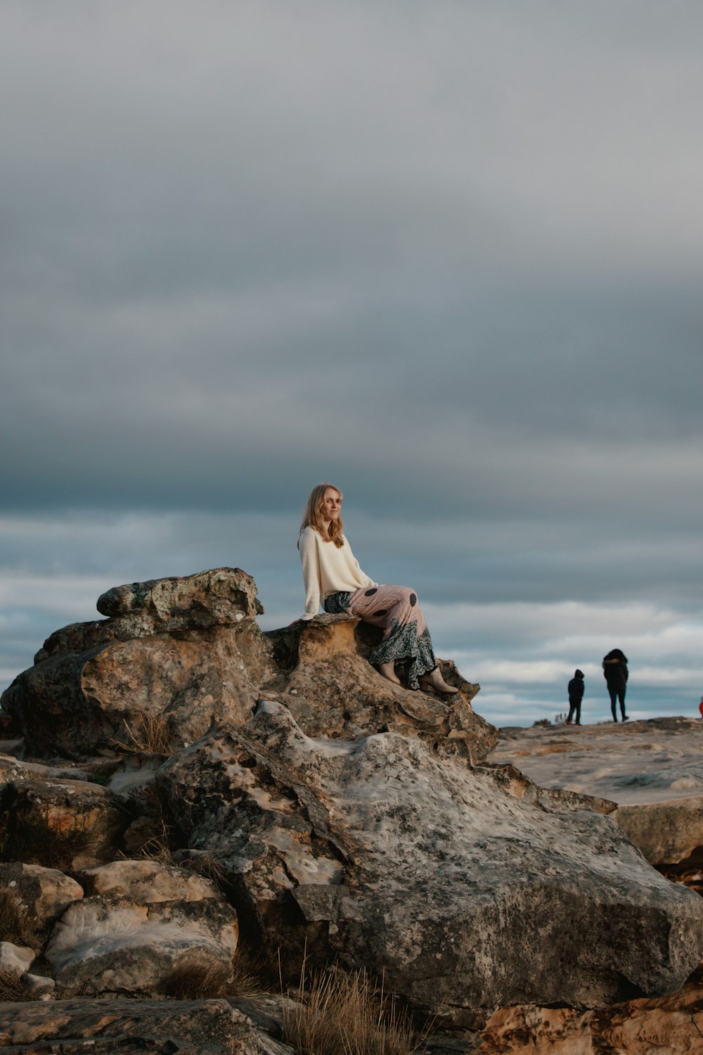 woman in white long sleeve shirt sitting on brown rock formation during daytime