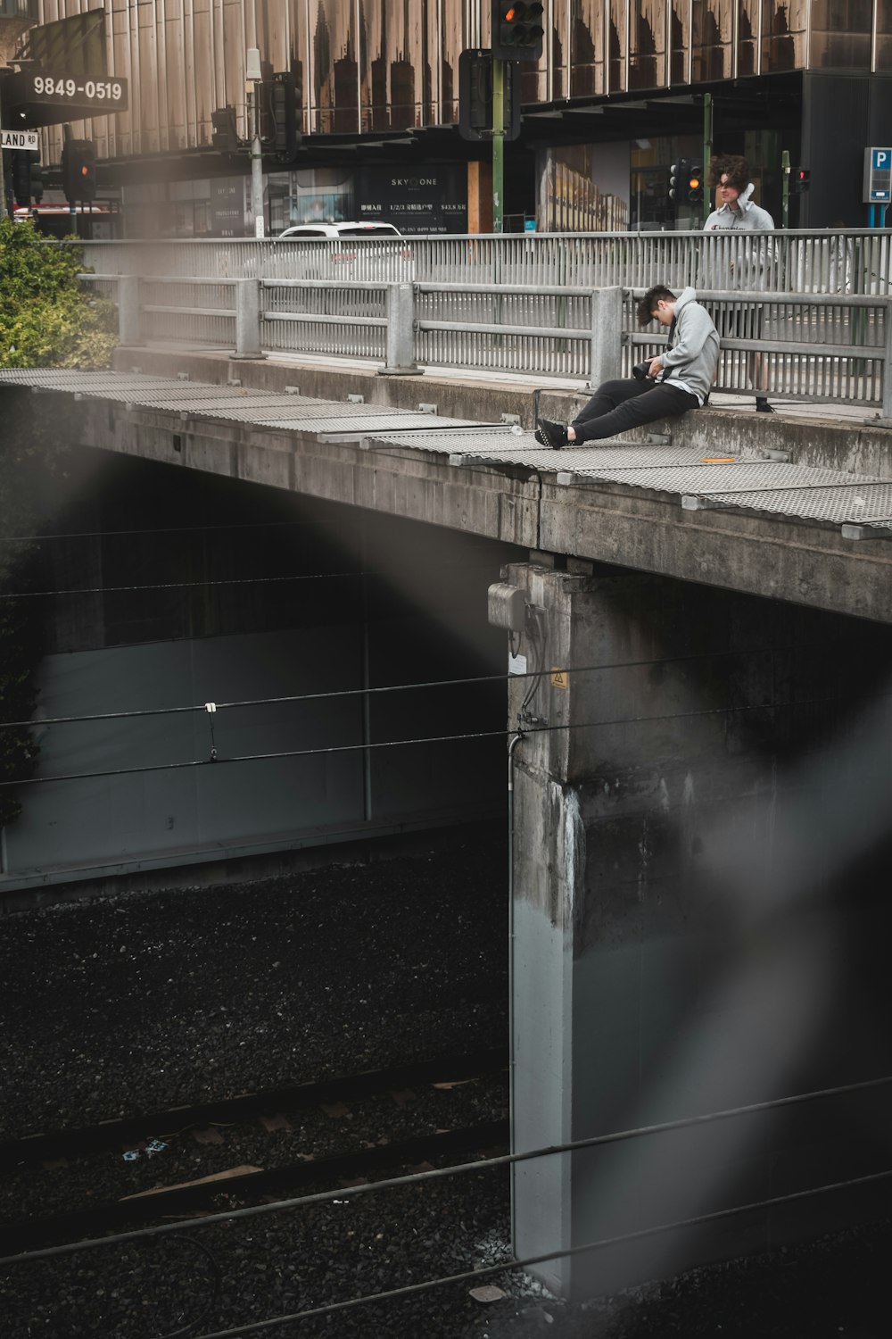 昼間、コンクリートの橋の上に座る白いシャツを着た男性
