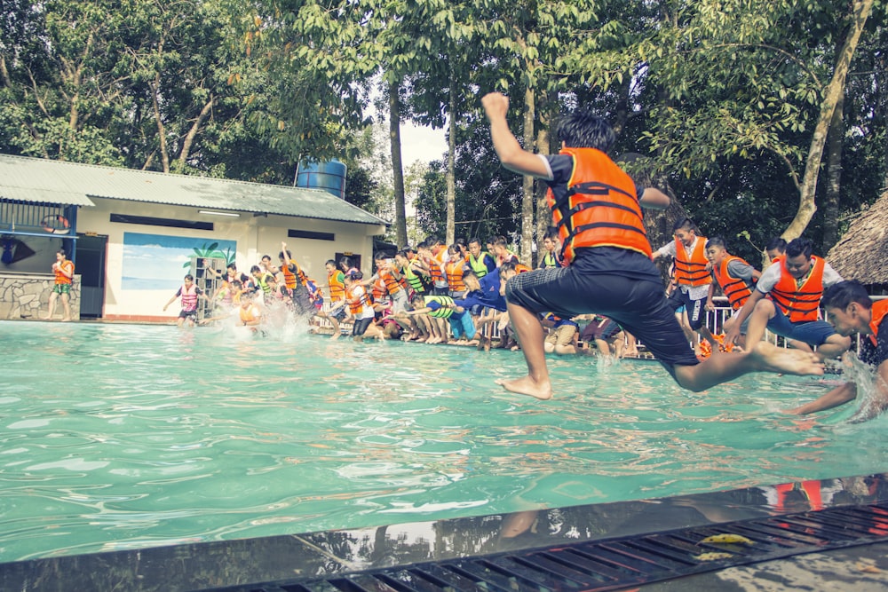 man in orange and black stripe shirt and black shorts jumping on pool during daytime