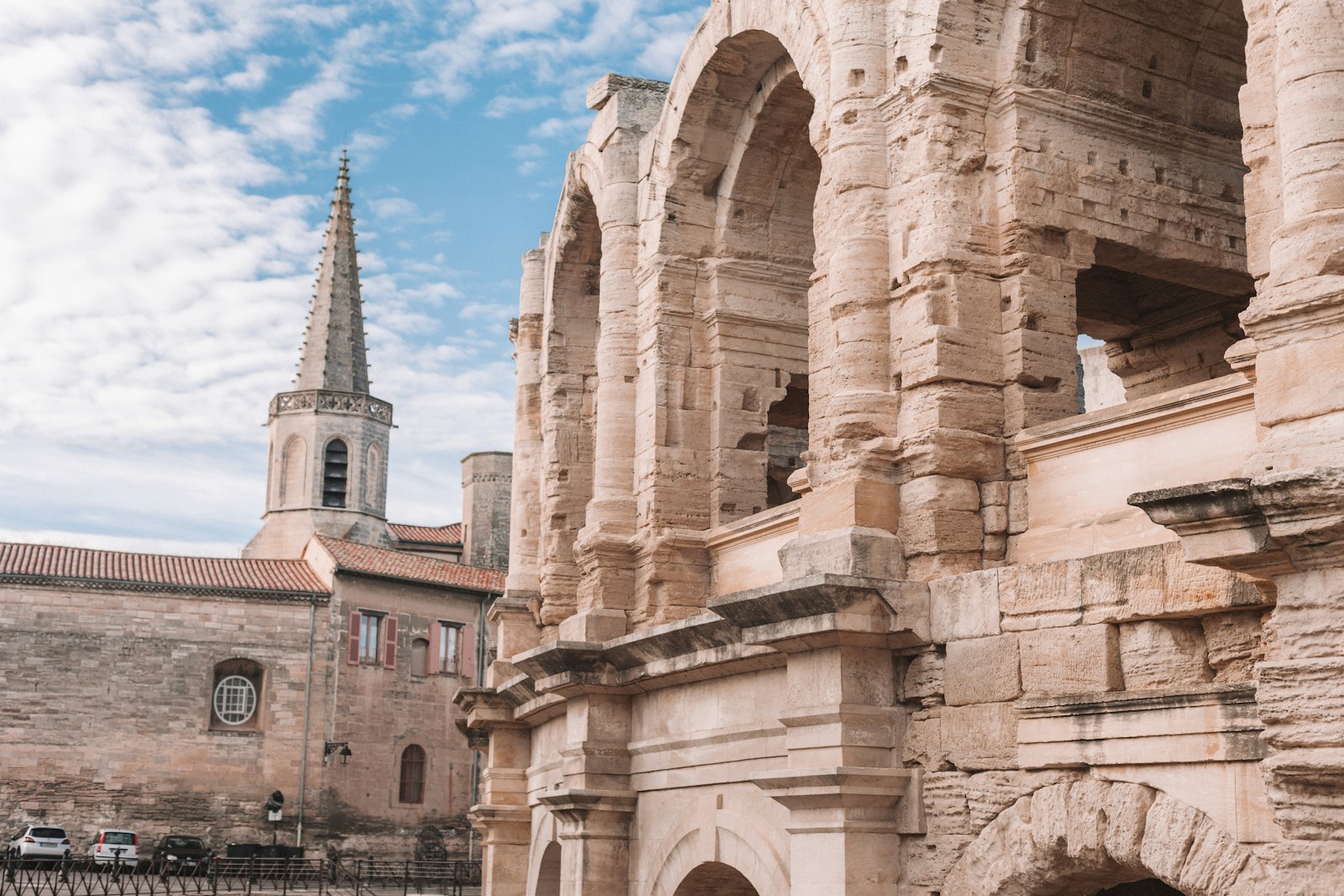 The stone arcades of the Roman amphitheater in Arles beside the bell tower of a neighboring church