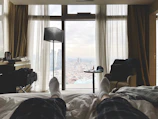 Cozy bedroom nook with layered textiles, a reading lamp, and cityscape visible through the window.
