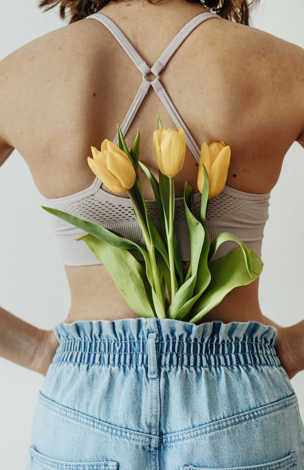 woman in blue and white stripe tank top holding yellow tulips