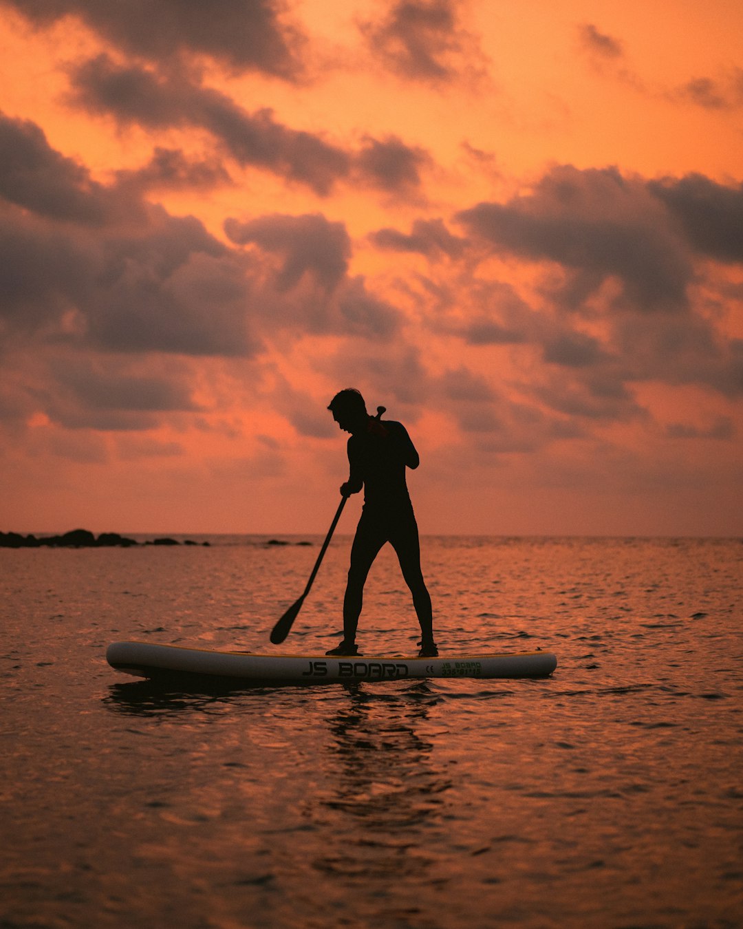 silhouette of man standing on surfboard during sunset