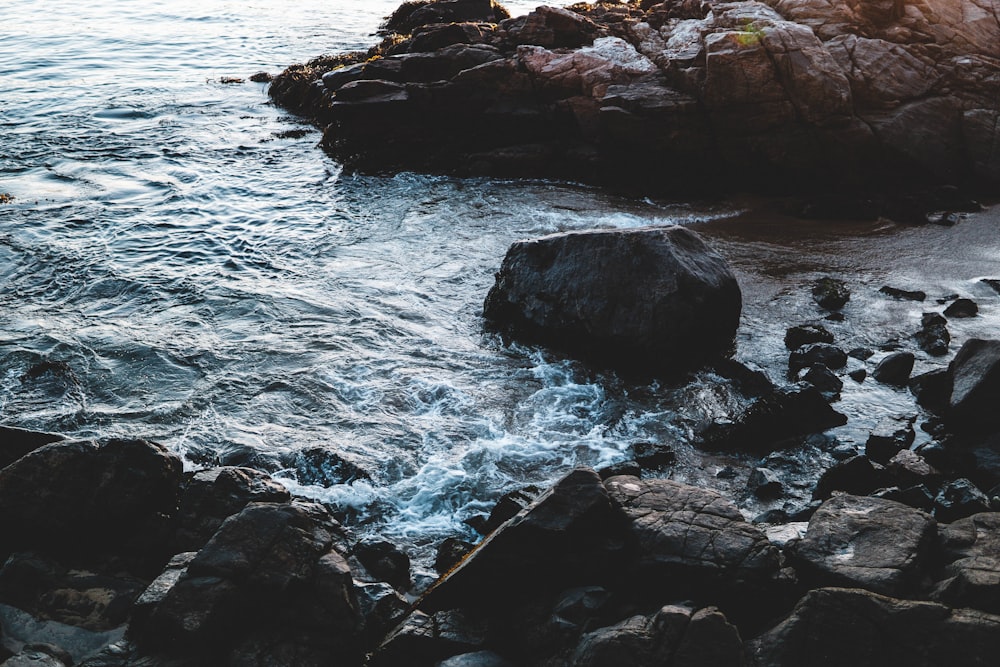 brown rocky shore with ocean waves crashing on rocks during daytime