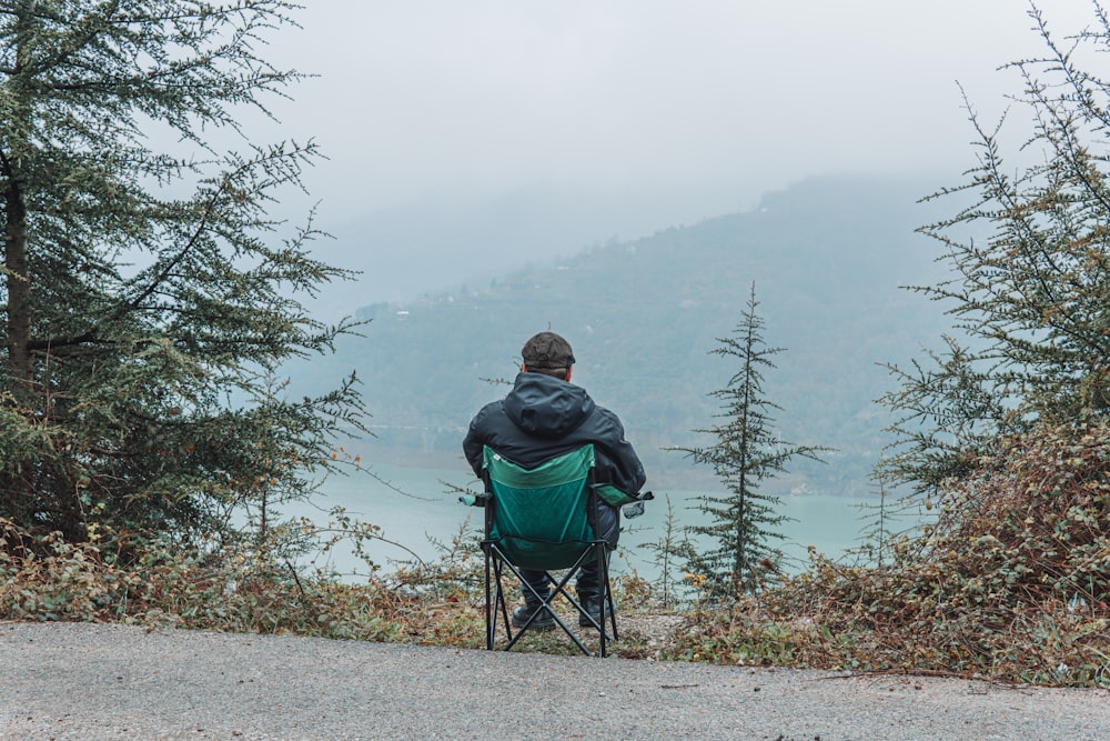 man in green jacket sitting on blue camping chair on gray dirt road during daytime