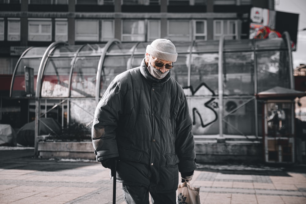 uomo in giacca nera e berretto a maglia che cammina sul marciapiede durante il giorno