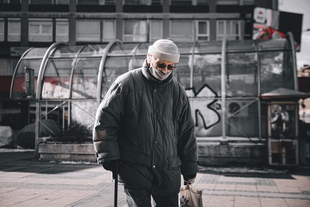 man in black jacket and knit cap walking on sidewalk during daytime