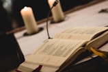 Sheet music and a Bible open on a wooden table with a candle.