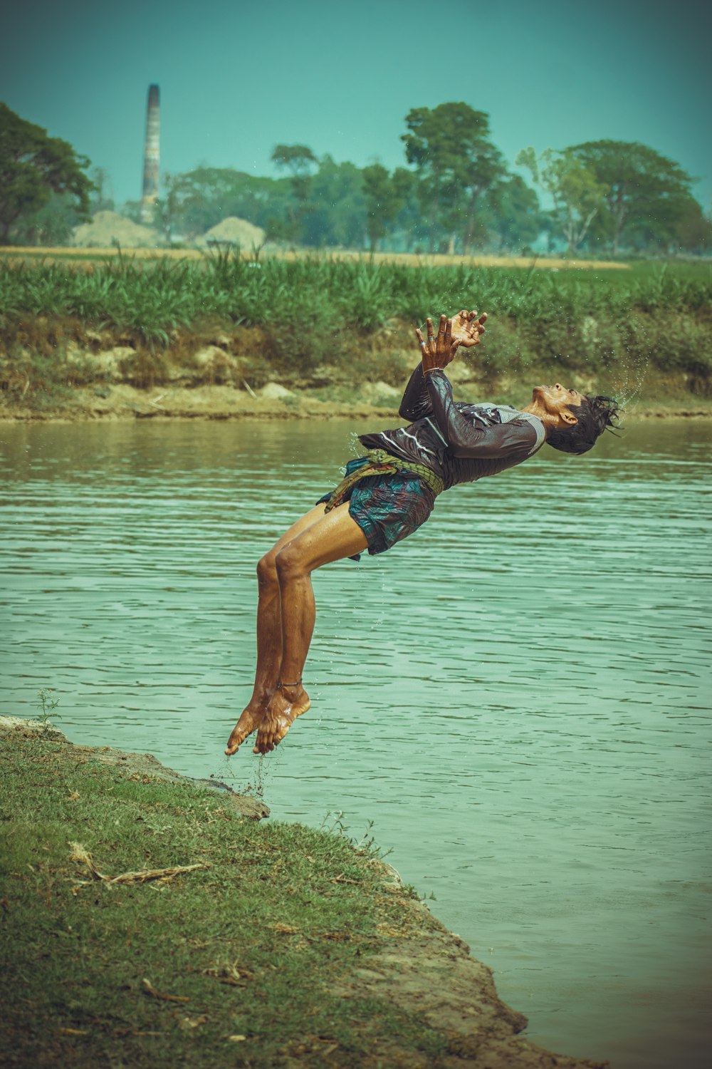 woman in black shirt and blue denim shorts sitting on rock by the lake during daytime