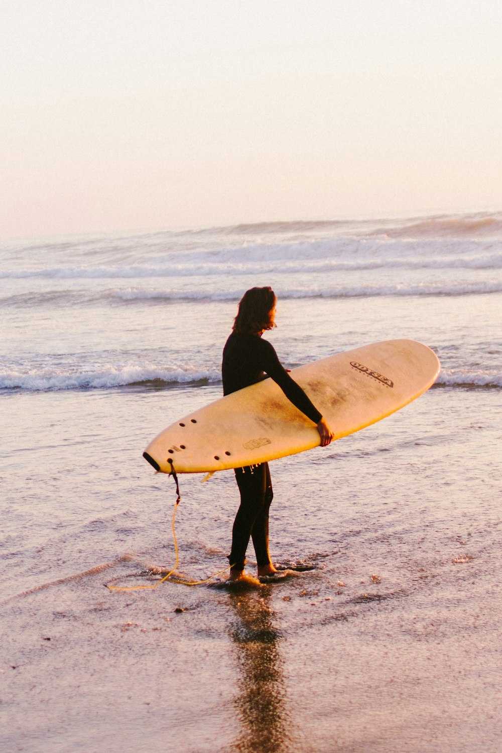 woman in black long sleeve shirt holding white surfboard walking on beach during daytime