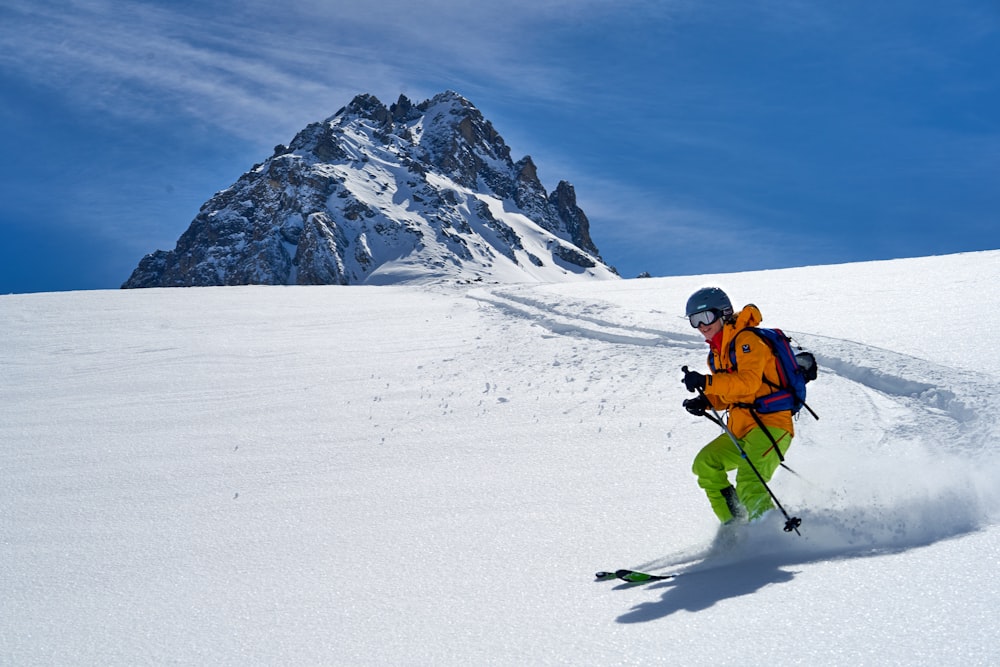 オレンジ色のジャケットと黒いズボンを着た男性が、昼間、雪に覆われた山でスキーブレードに乗っている