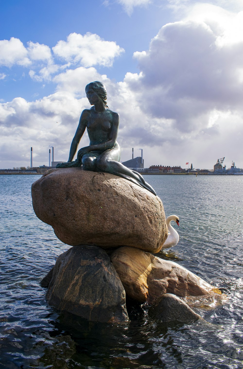 statue of man sitting on rock near body of water during daytime