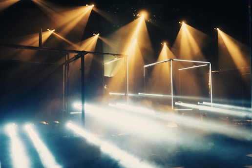 Dramatic lighting with multiple beams of light and geometric structures. The lights create a mysterious and dynamic atmosphere, with smoke adding depth and texture.