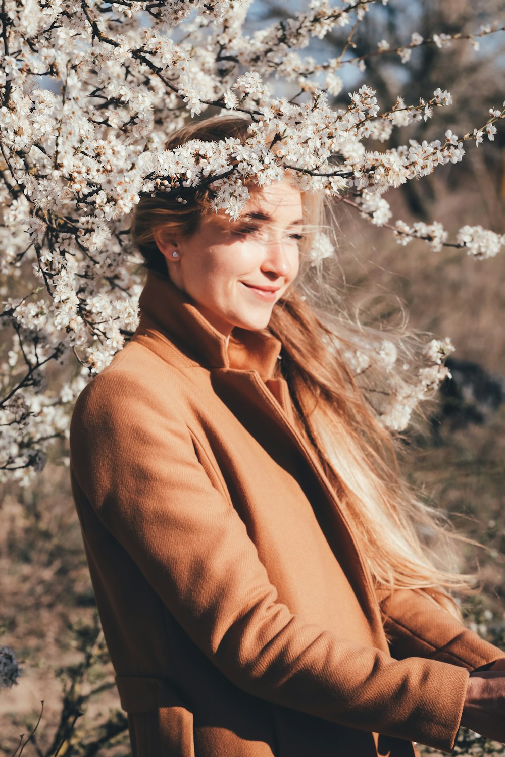 woman in brown coat standing near white flowers during daytime