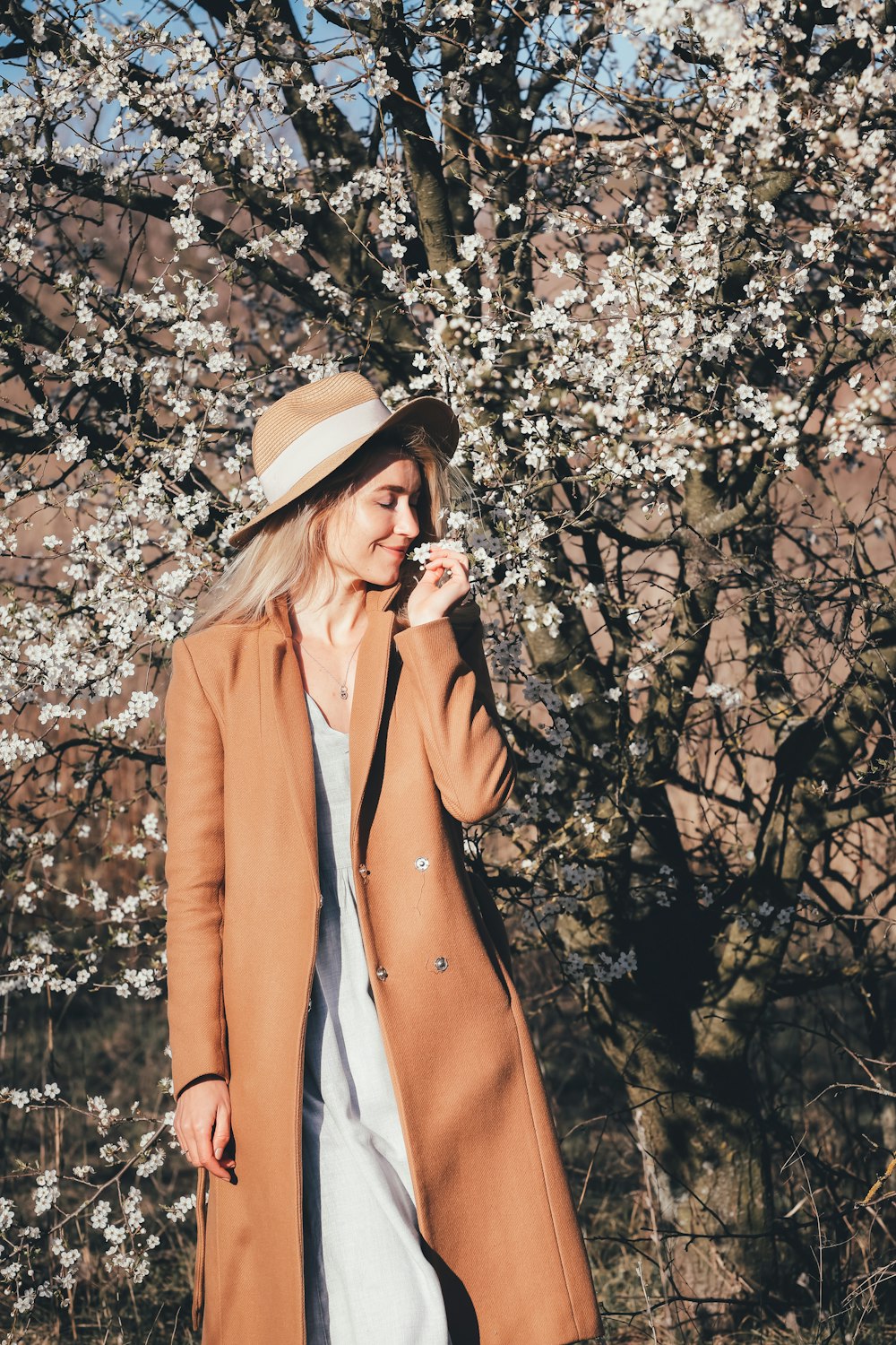 woman in brown coat wearing brown hat standing near brown leaf tree during daytime
