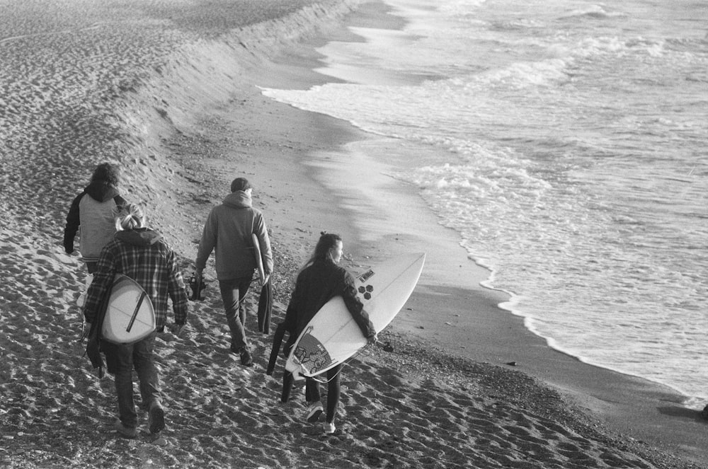 grayscale photo of man and woman holding surfboard walking on beach