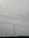 A large metal electricity transmission tower stands amidst a landscape, towering over a series of power lines stretching wide across the frame. The horizon features a slight silhouette of hills in the distance under a cloudy sky.