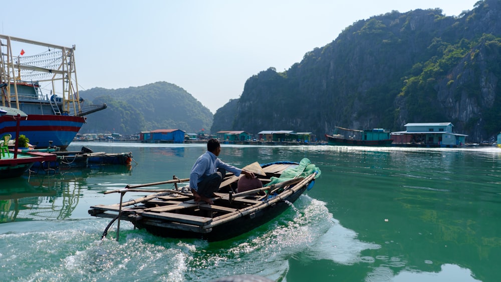 Mann im weißen Hemd sitzt tagsüber auf braunem Boot auf Gewässer