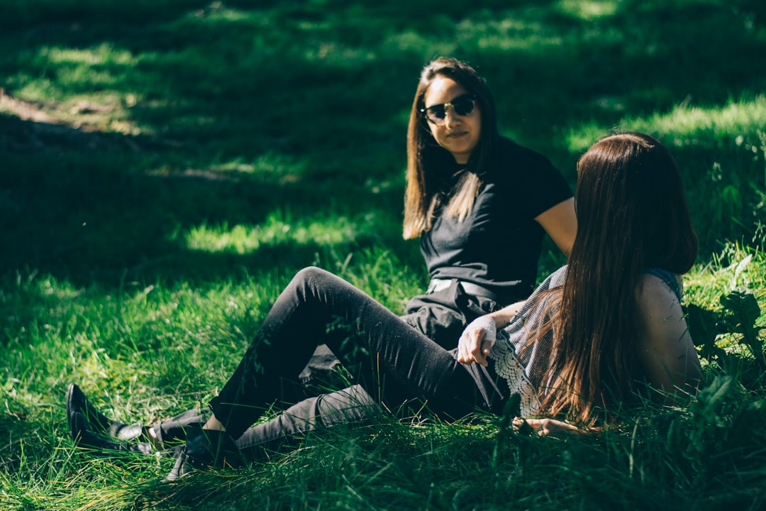 woman in black shirt and black pants sitting on green grass during daytime