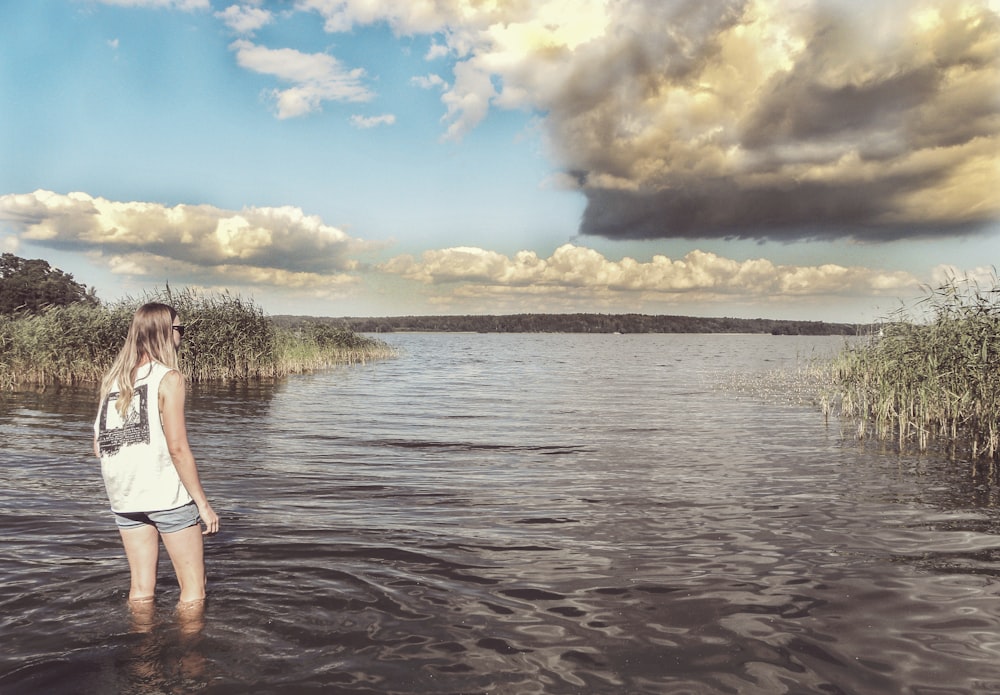 woman in white tank top and blue denim shorts standing on seashore during daytime