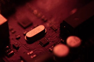 A close-up of an electronic circuit board illuminated with a red light, highlighting various components such as capacitors and integrated circuits.