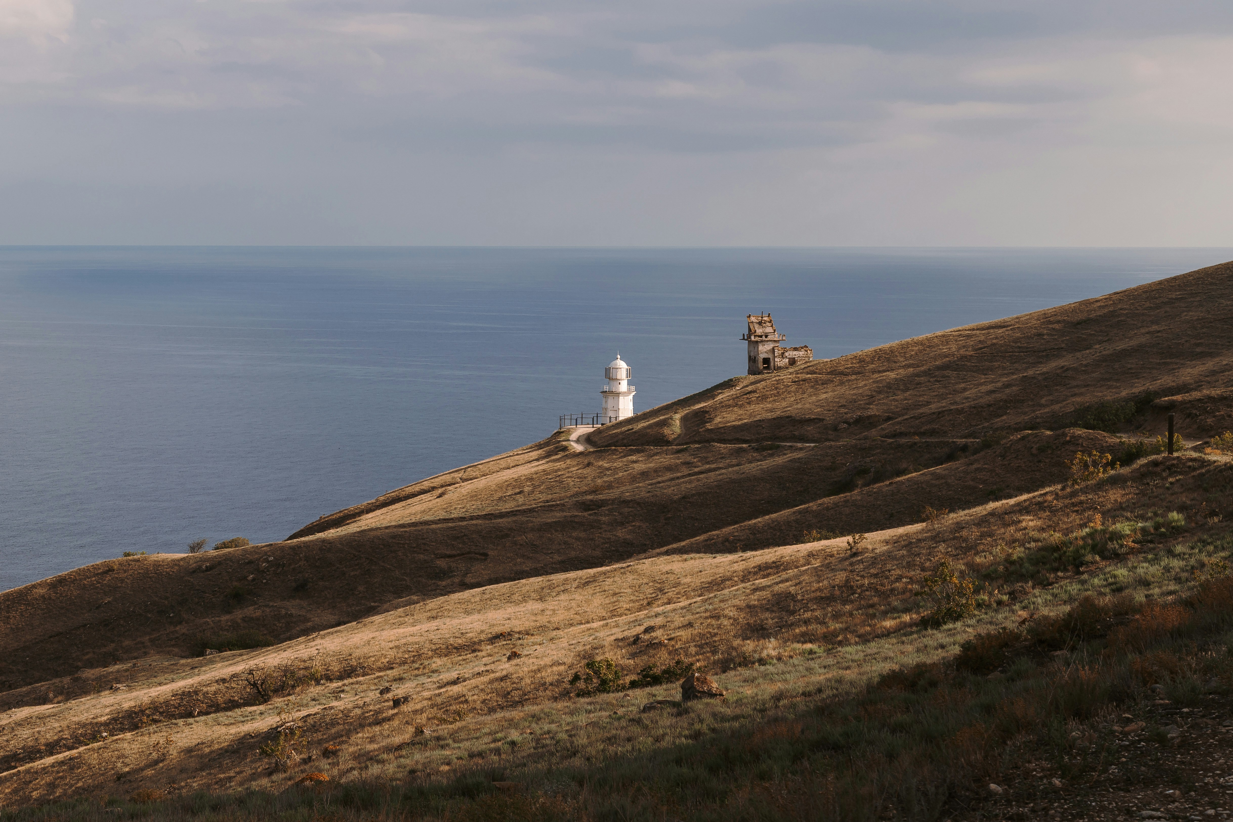 white lighthouse on brown hill near body of water during daytime