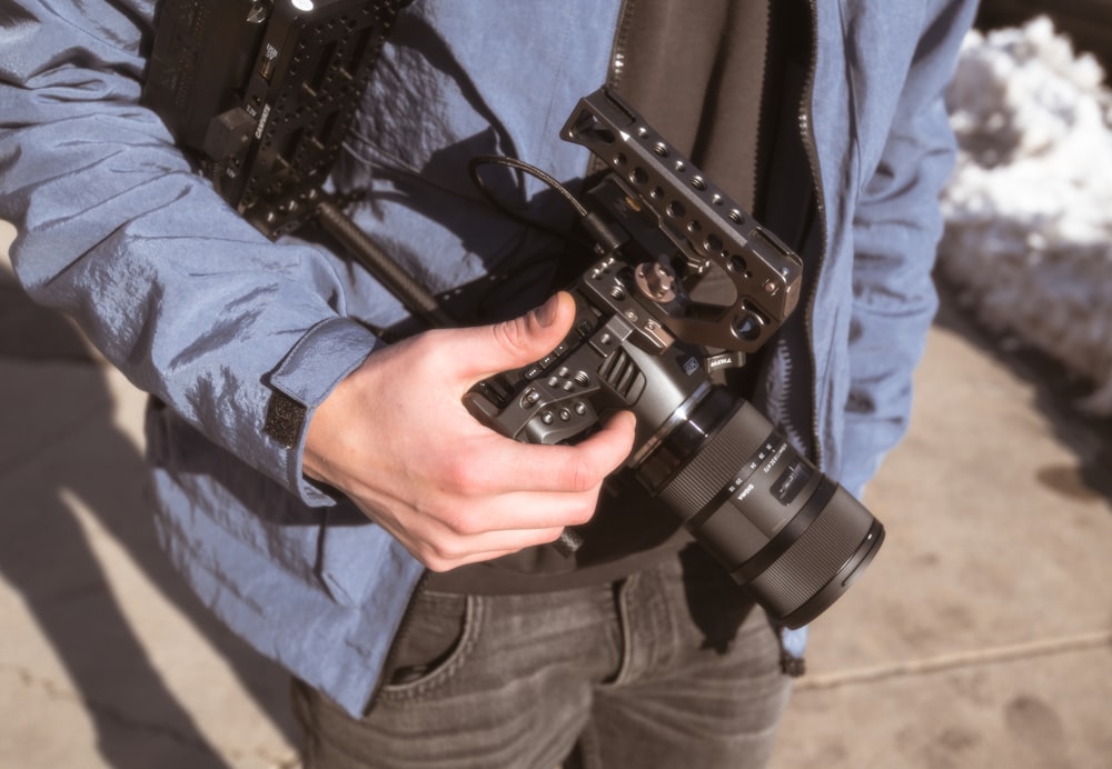 Persona in giacca blu che tiene in mano una fotocamera DSLR nera