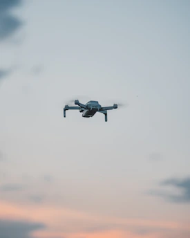 A sleek drone hovering against a clear baby blue sky with hints of orange sunset.