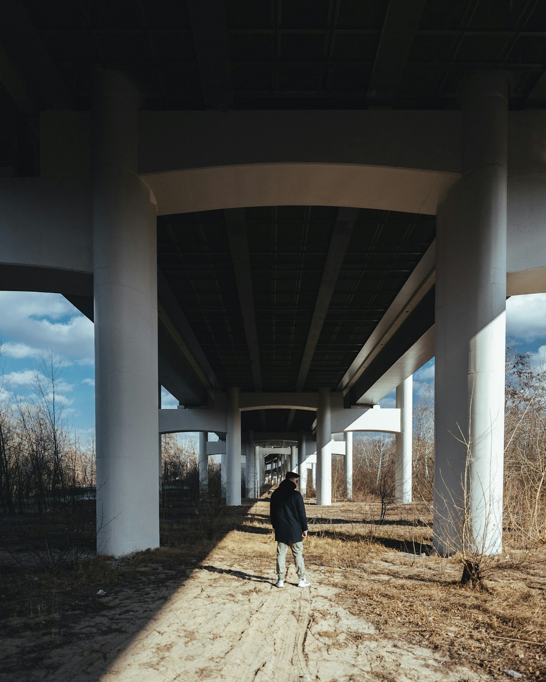 person in black jacket walking under brown concrete bridge during daytime