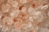 A close-up view of variously sized pink and white crystals, resembling salt or mineral stones. The textures appear rough and granular, with some stones exhibiting a translucent quality.