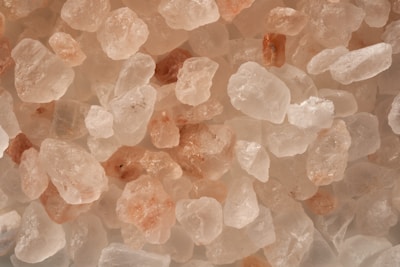 A close-up view of variously sized pink and white crystals, resembling salt or mineral stones. The textures appear rough and granular, with some stones exhibiting a translucent quality.