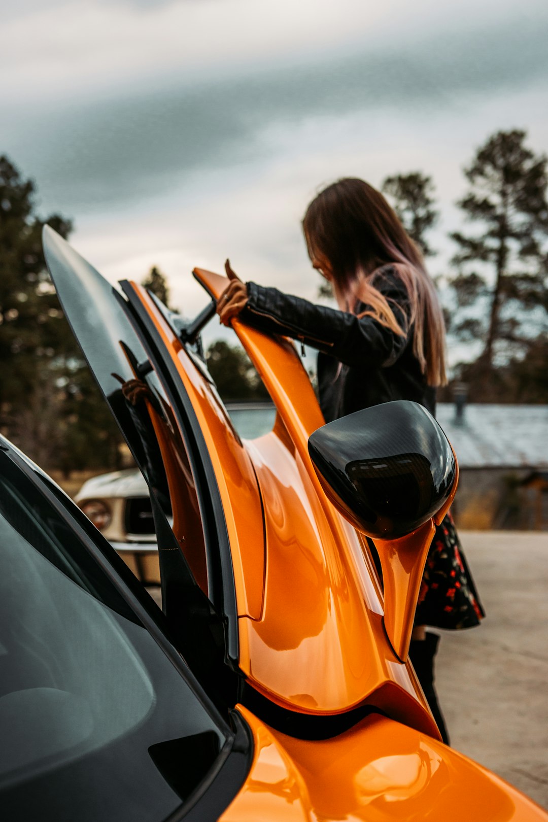 woman in black jacket leaning on orange car during daytime