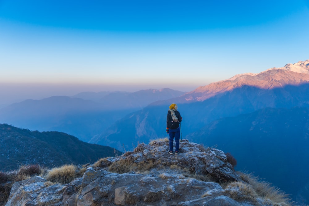 man in black jacket standing on rock mountain during daytime