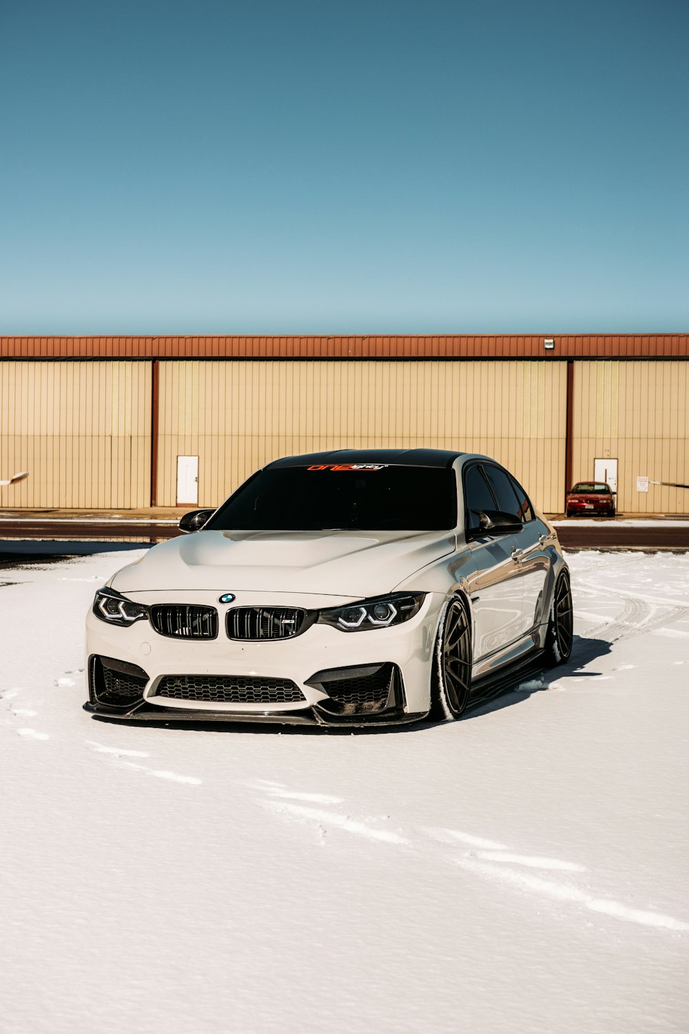 昼間、雪に覆われた地面に駐車された白いBMW M3クーペ